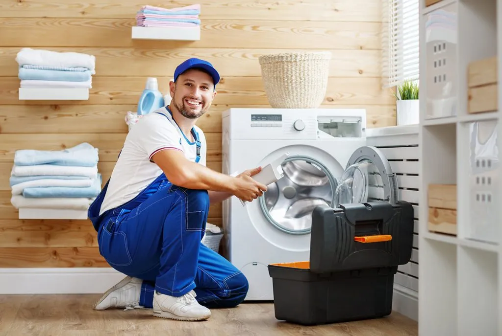 working man plumber repairs a washing machine in laundry