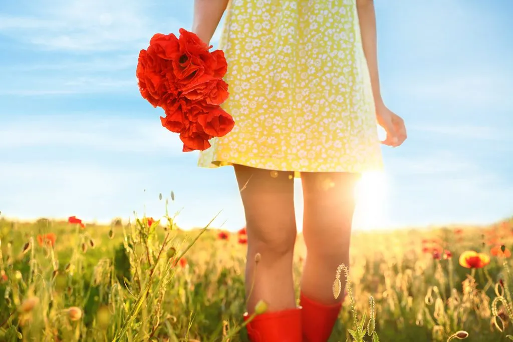 in a sunlit field, a woman wearing red boots holds a bouquet of poppies