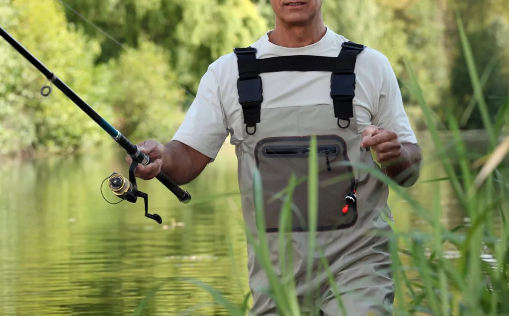 In a river, a man is fishing while wearing chest waders