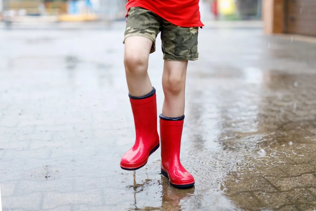 child wearing red rubber boots has fun splashing water