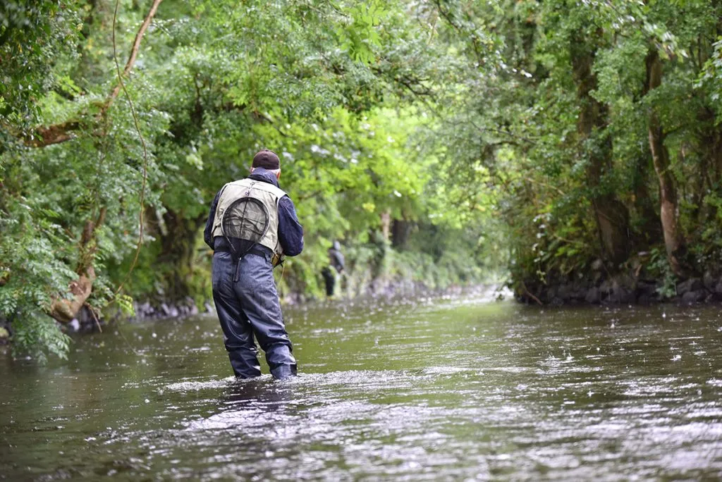 back view of a fly-fisherman fishing in a river while wearing a waterproof wader