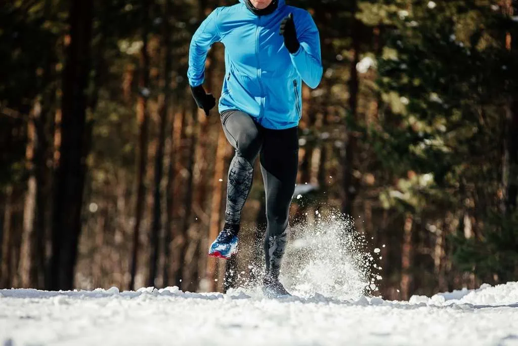 runner in leggings running winter trail snow flies spray