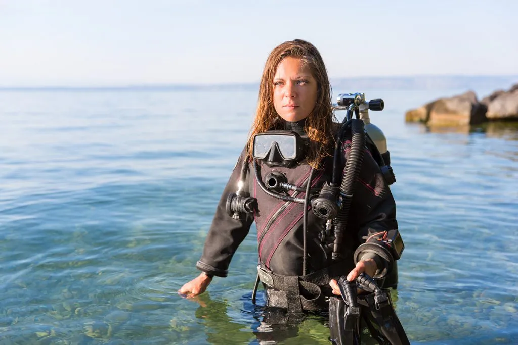 female scuba diving instructor standing in water wearing a dry suit