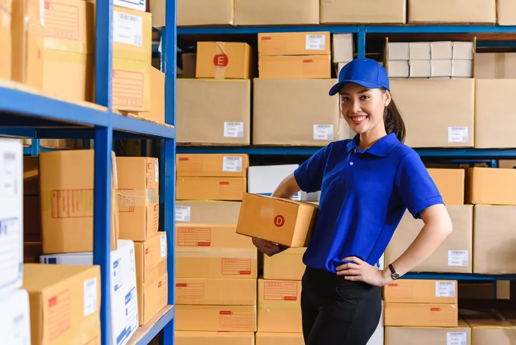 in a warehouse, a woman in blue uniform holds a parcel box size D