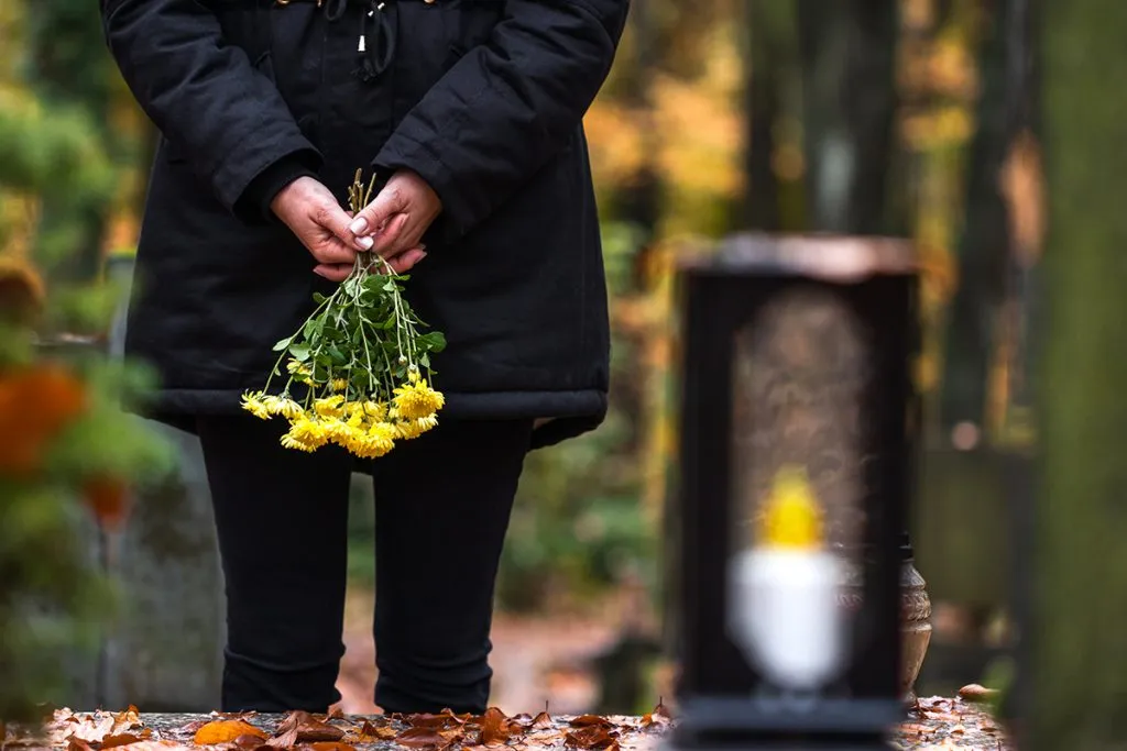 mourning woman stands at a cemetery grave with flowers in her hands