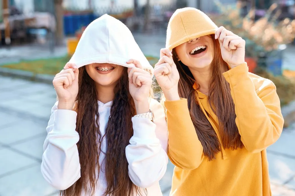 two women in bright colored hoodies walking, laughing and posing on the street