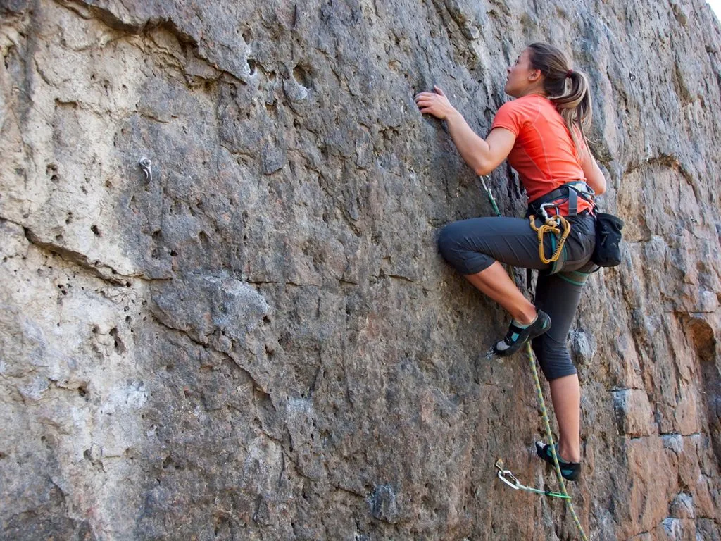 woman wearing leggings with a rope engaged in the sport of rock climbing on the rock
