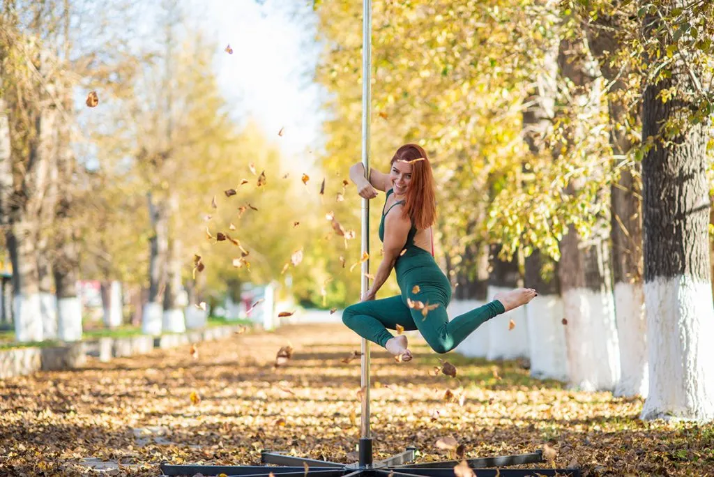 woman wearing leggings dances on a portable pole stage against the backdrop of autumn leaf fall
