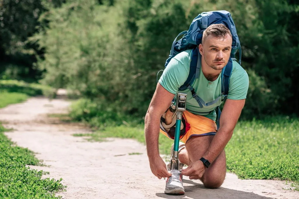 confident man with physical disorders adjusting his shoelaces while walking outdoors