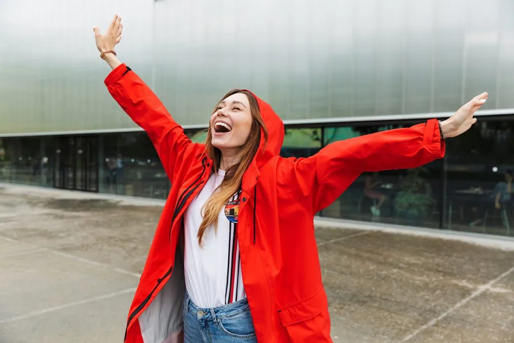 young happy woman in a raincoat poses outside