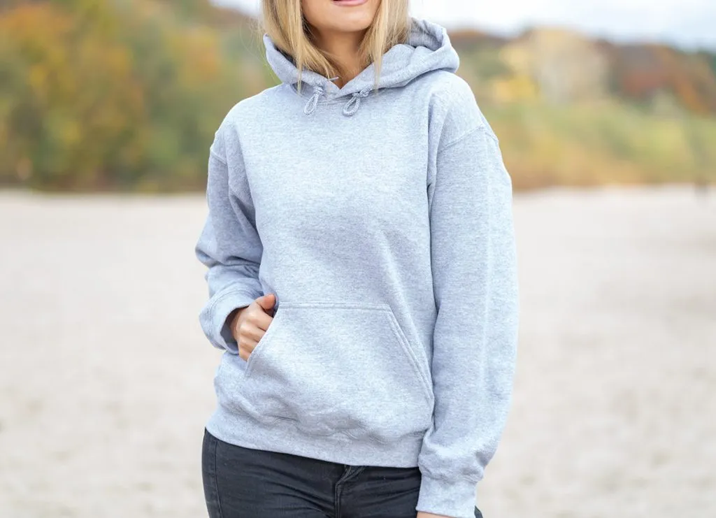 blond woman is standing on the beach, wearing a light grey hoodie