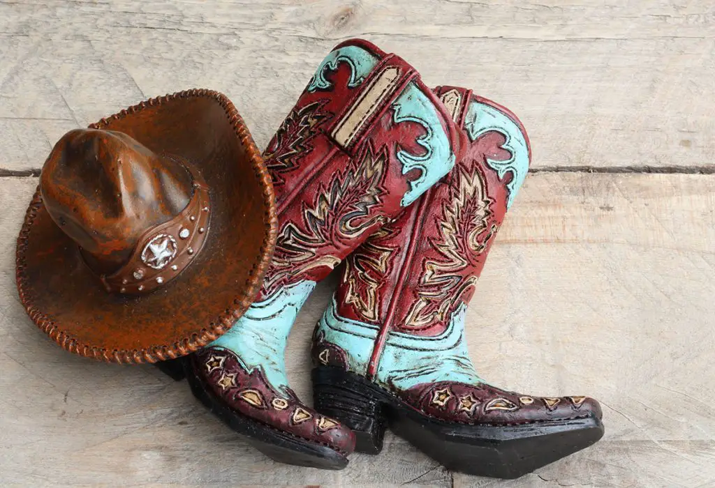 pair of cowboy boots with a cowboy hat close up laying on a wood