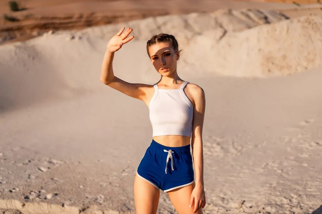 girl in a sexy white top and short shorts stands in the desert and covers her eyes with the hand from the sun