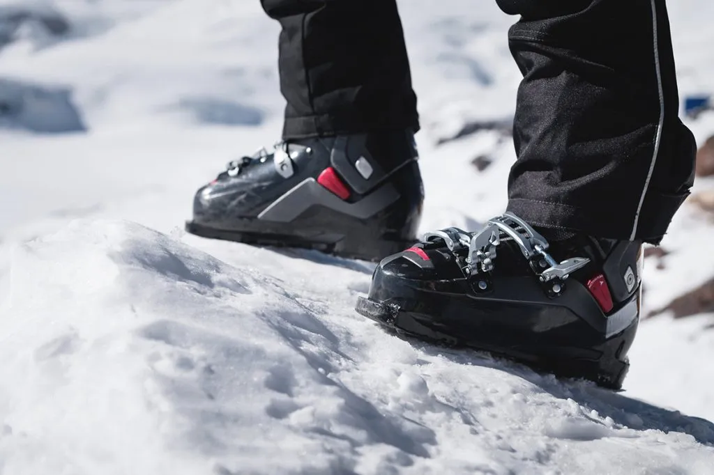 a skier's leg in ski boots without skis stands on a knoll of bliss against the background of mountains on a sunny day. The concept of skittura and hiking ski travel