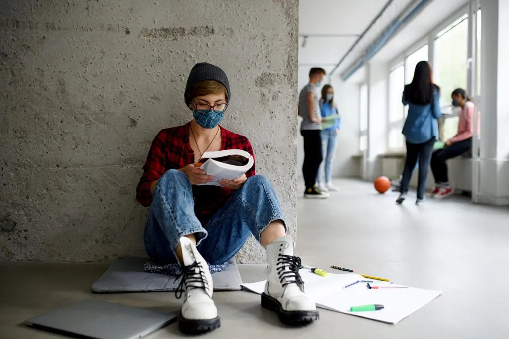 student with face mask and boots sitting on floor back at school