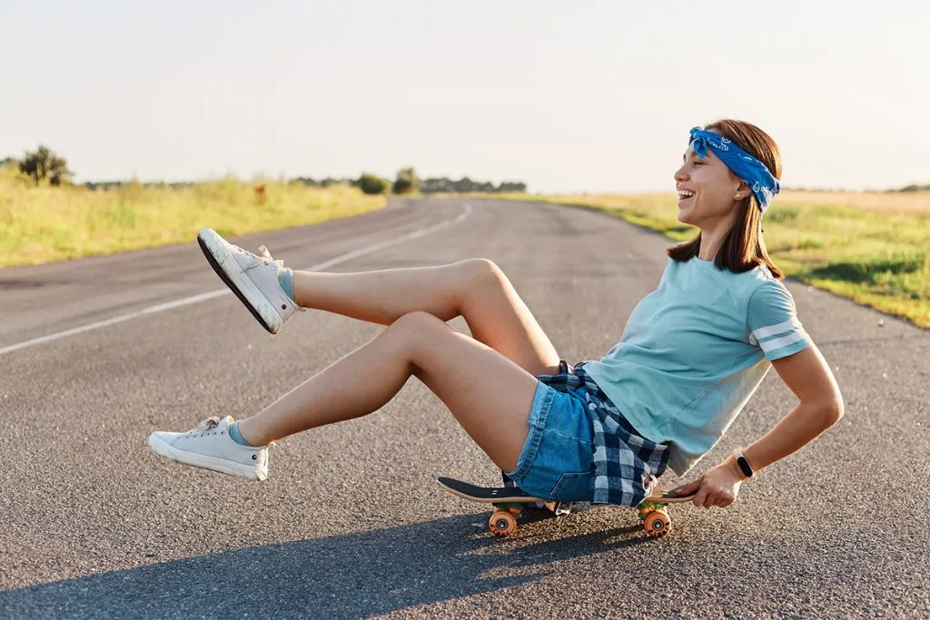 woman sitting on skateboard on the street with raised legs