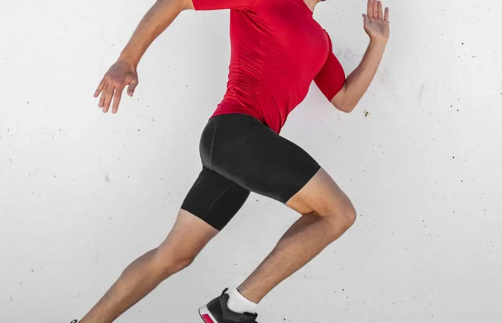 run race athlete running man sprinting fast profile sideways against white wall outdoor background. Male runner training glutes and legs muscles