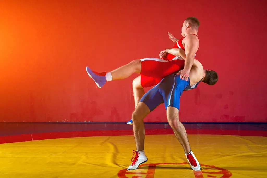 wrestlers in red and blue uniform short wrestling on a yellow wrestling carpet in the gym