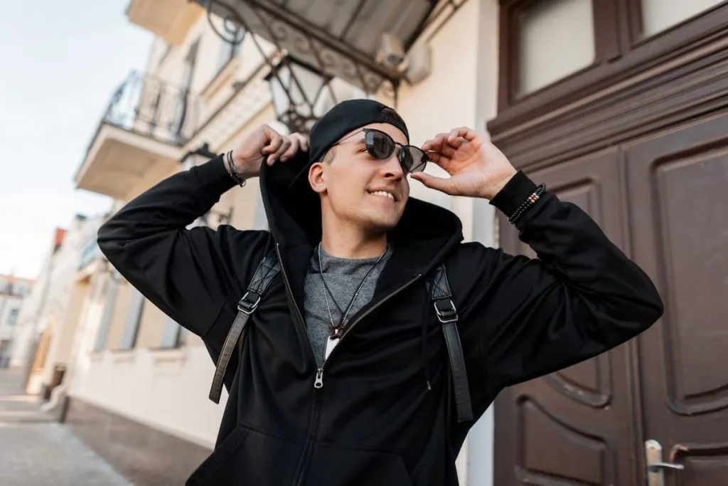young happy hipster man with a cute smile in a fashionable black hoodie cap, sunglasses, and backpack