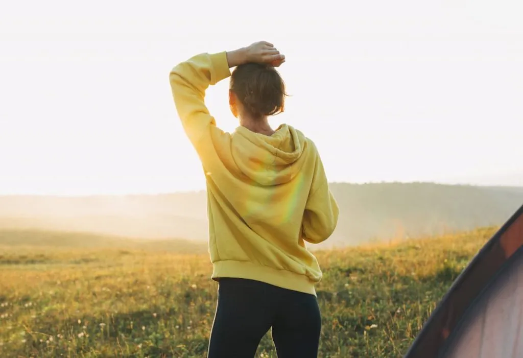 young woman traveler in yellow hoodie looking at sunrise on beautiful view