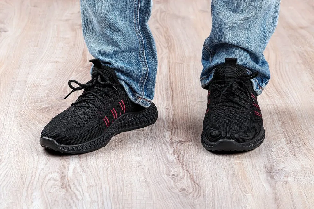 man in blue jeans and black shooes standing on a light brown floor