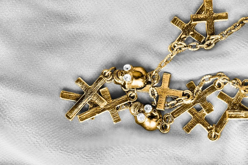 gold chain with crosses and skulls pendants on white textile background