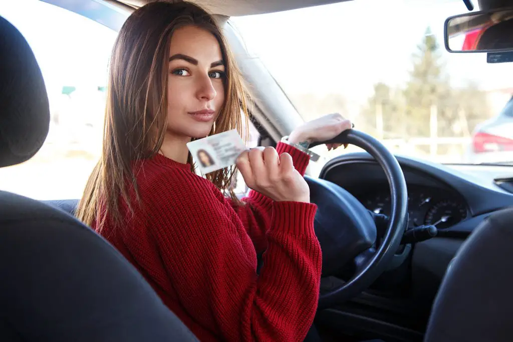 girl driving car with a drivers license card in her hands