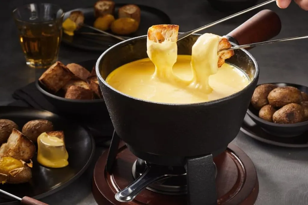 delicious cheese fondue with dipping forks coated in melted cheese surrounded by assorted breads and potatoes