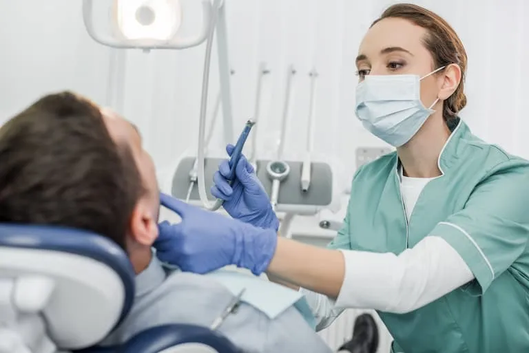dentist in mask holding dental instrument and touching face of patient in dental clinic