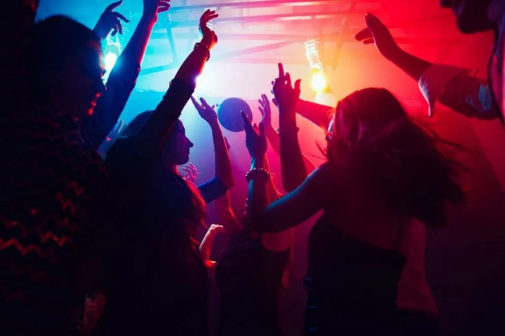 a crowd of people raises their hands on dancefloor on neon light