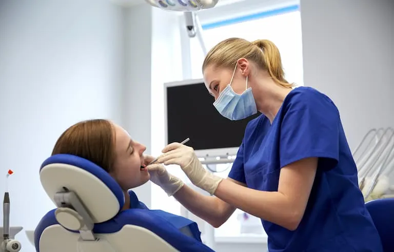 female dentist with mirror checking patient girl teeth up at dental clinic office