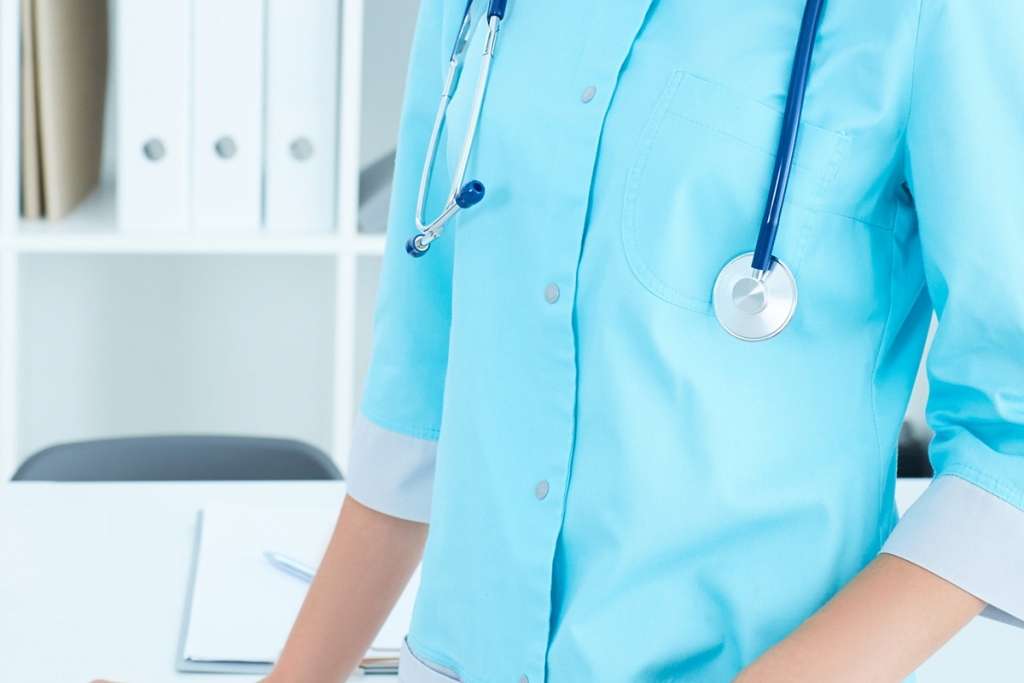 female in scrubs standing, rests her hand on the table in her office