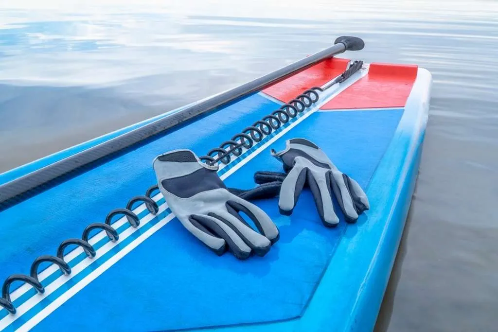 paddling gloves, safety leash, and paddle on a deck of a stand-up paddleboard