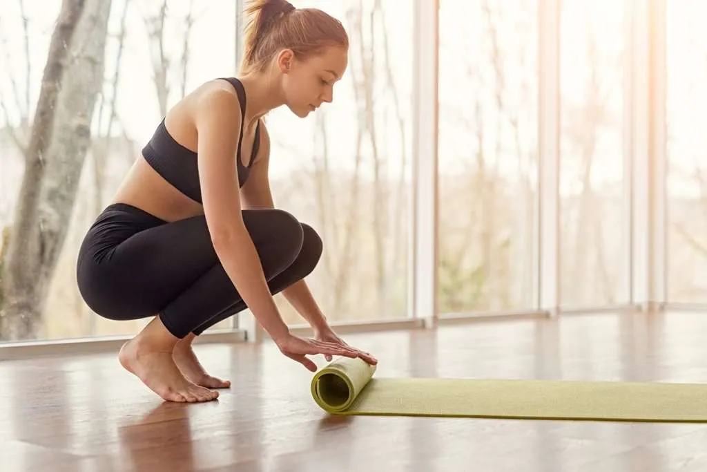 slim lady in leggings is rolling her yoga mat