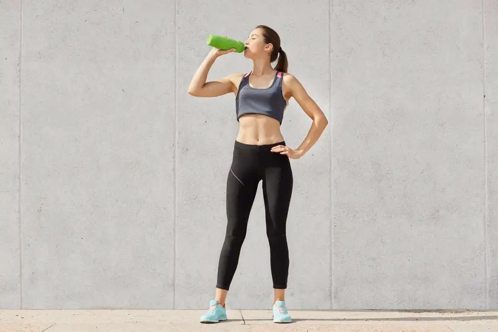 thirsty woman dressed in leggings drinks water