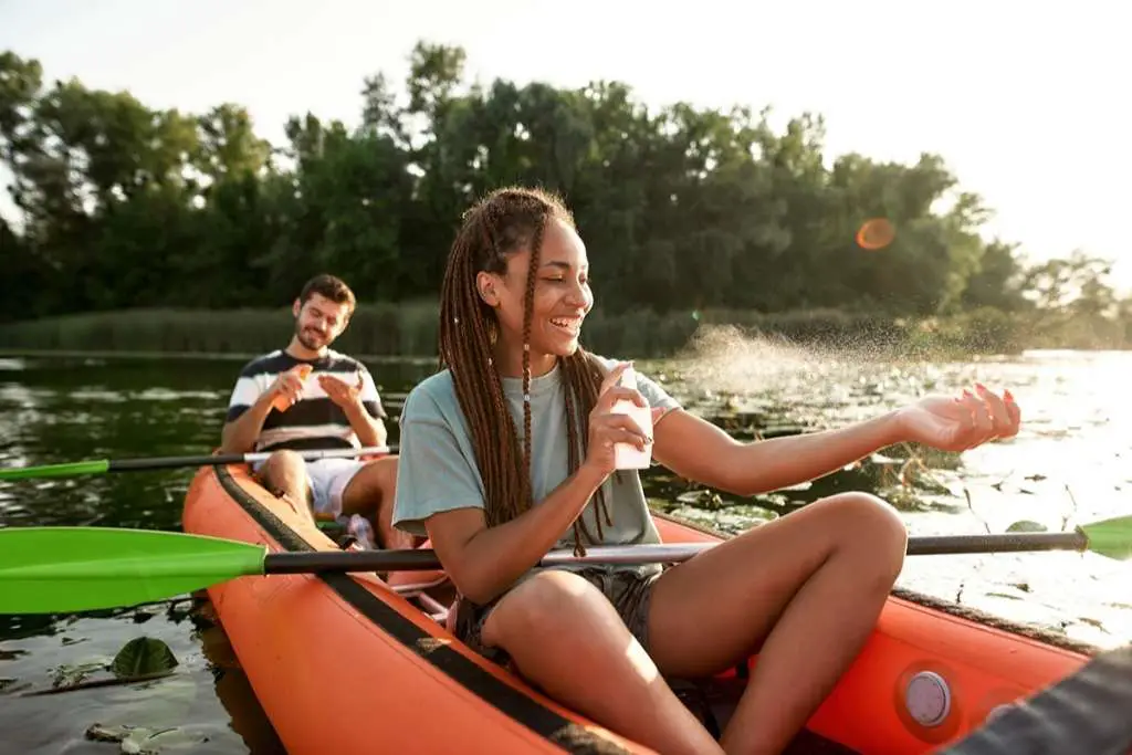 woman spraying sunscreen protection while kayaking on the river with her boyfriend outdoors