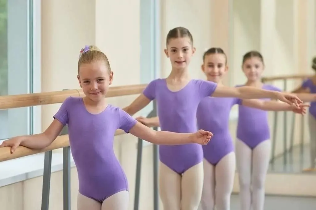 young ballerinas standing near ballet barre